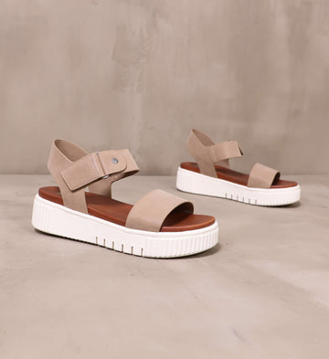 pair of taupe straps and white soles on the sole mate platform sandals angled on cement background