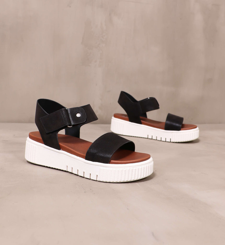 black straps and chunky white platform soles on the sole mate platform sandals angled on cement background