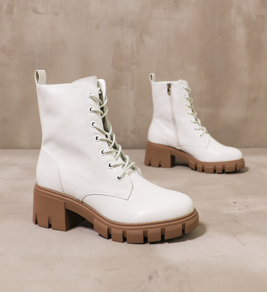 pair of white speed of white boots with brown lug soles angled on cement background