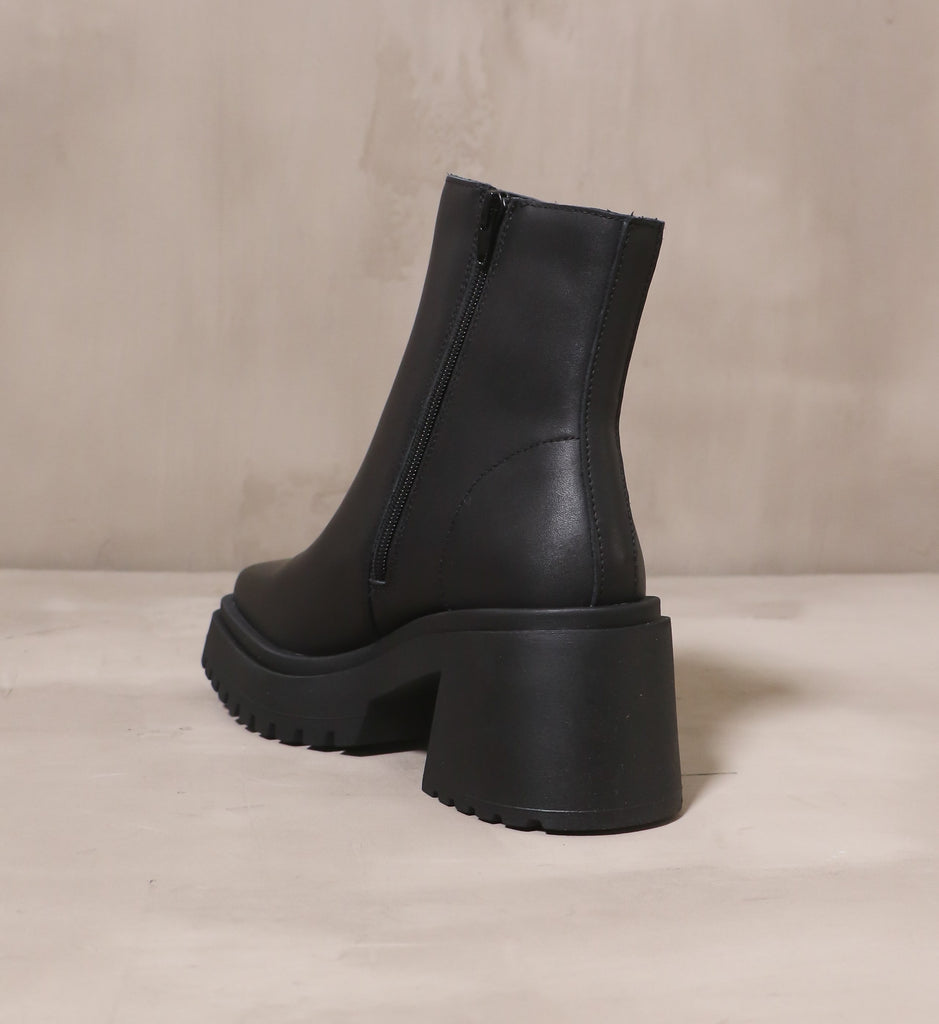 back of the chunky rubber block heel on the black steve madden shadow of a doubt boot on cement background
