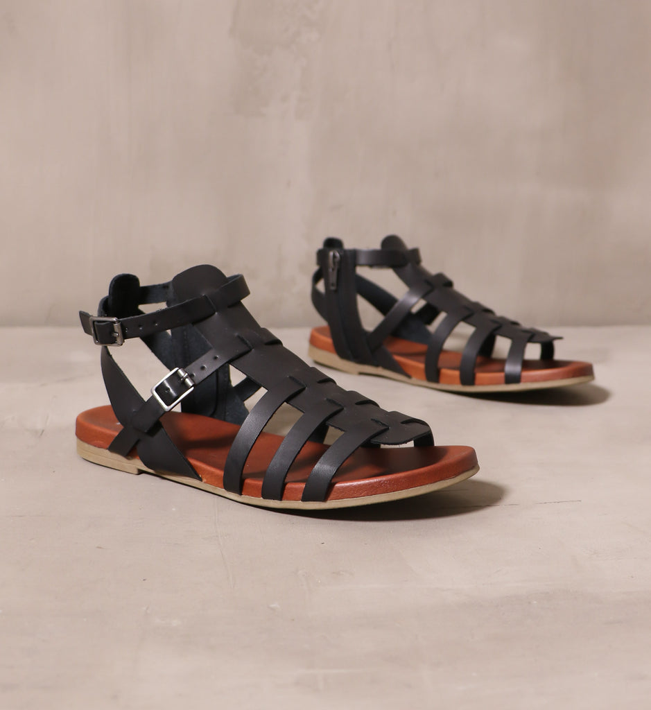 pair of black leather strappy makes me happy sandals on cement background