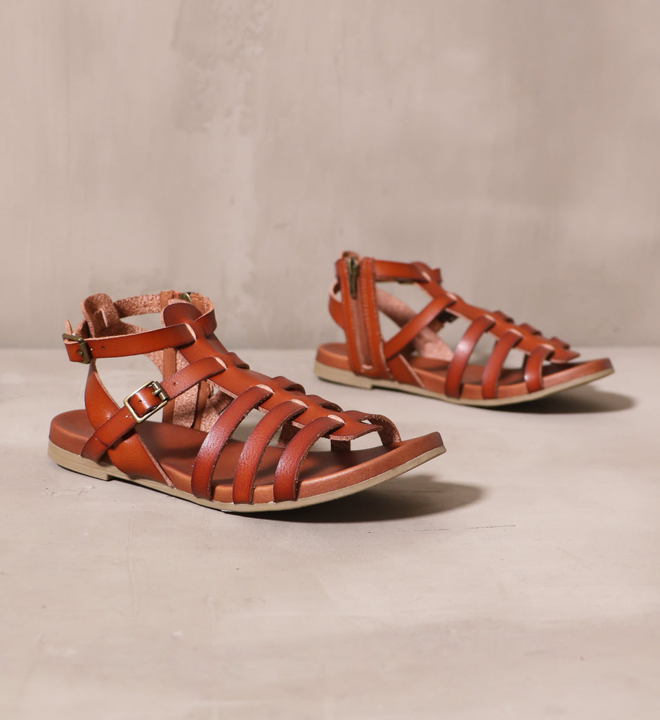 pair of cognac tan strappy makes me happy leather cage sandals on cement background