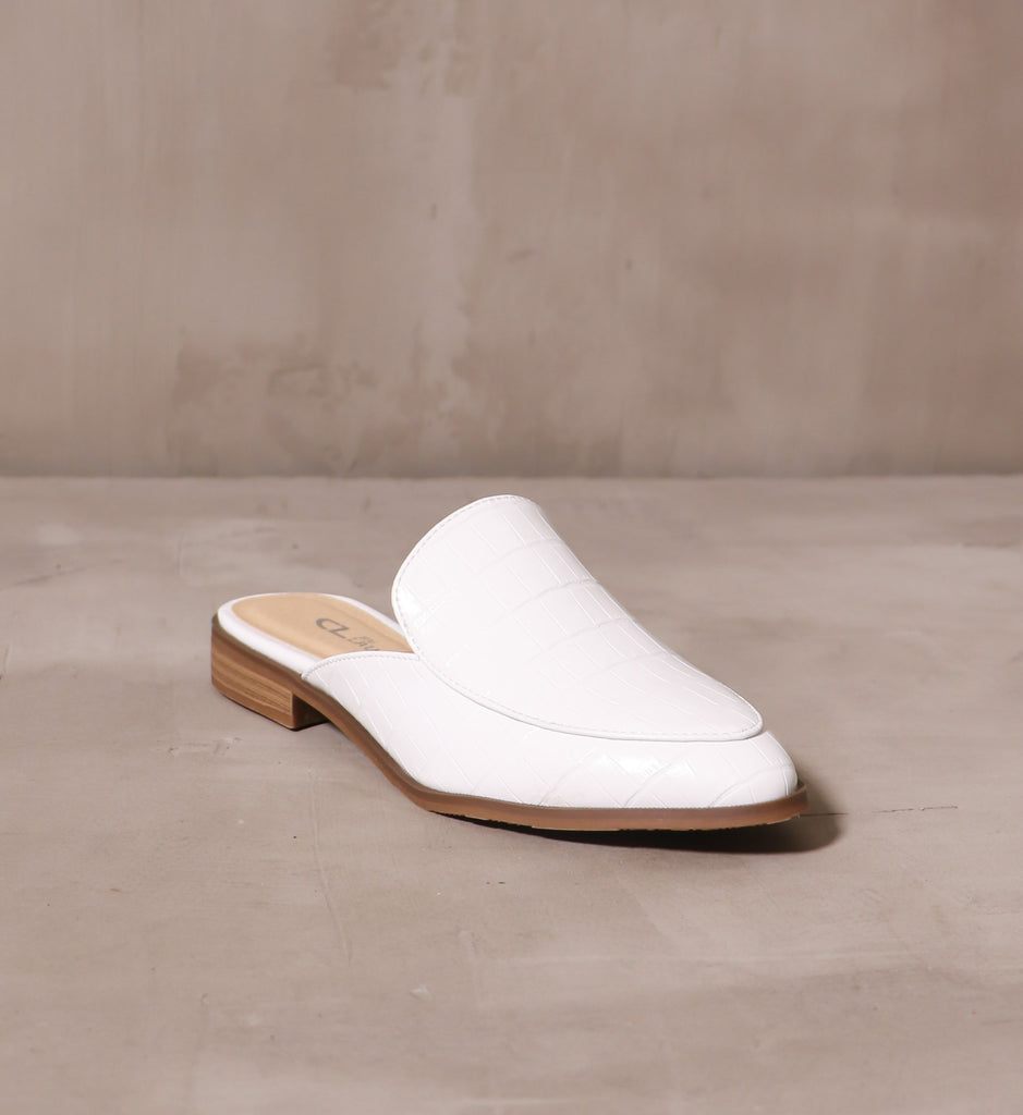 closed almond toe sugar and spice mules with white upper and brown sole on cement background