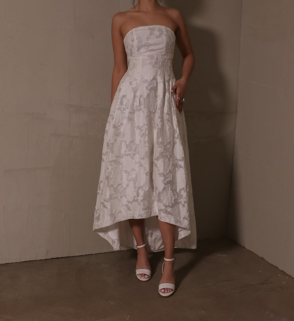 model standing on concrete floor wearing strapless white floral gown and open toe pop the cork heels